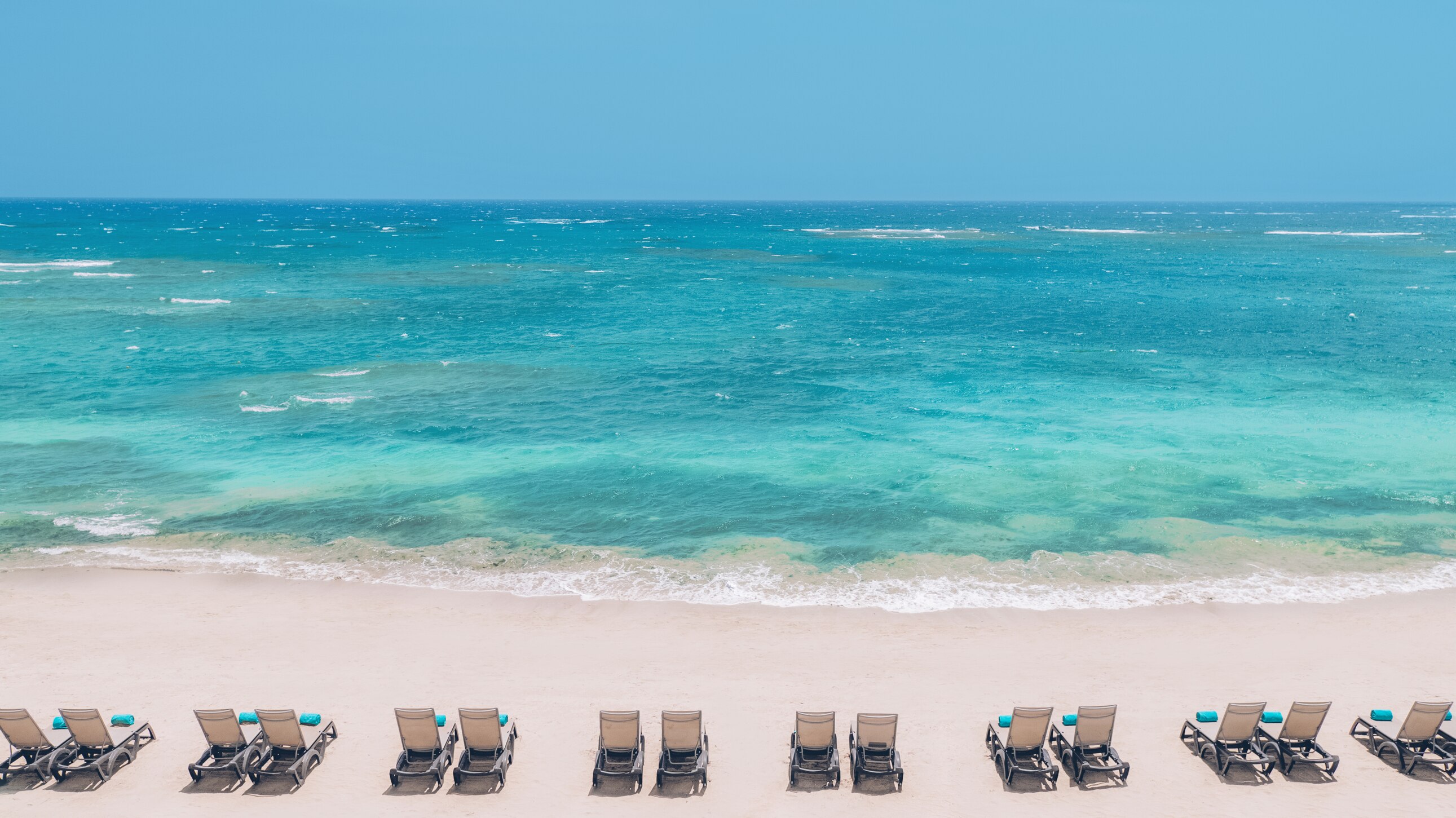 Empty lounge chairs facing turquoise ocean beach